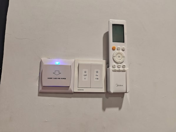 Un panel de control instalado en la pared con una ranura para tarjeta, un interruptor para el ventilador y un control remoto.