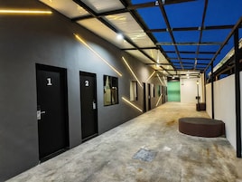 Un pasillo con puertas numeradas, una pantalla verde y suelo de hormigón.