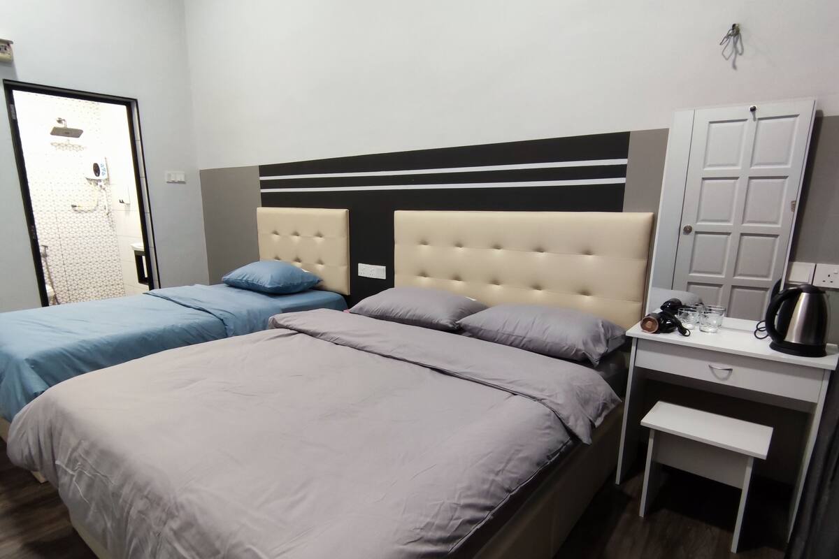 A hotel room with a large bed, two smaller beds, a desk with a kettle, and a wardrobe.