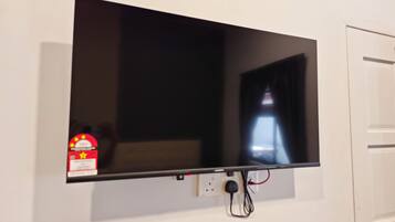 A flat-screen TV mounted on a white wall, with a power outlet and cables below it.