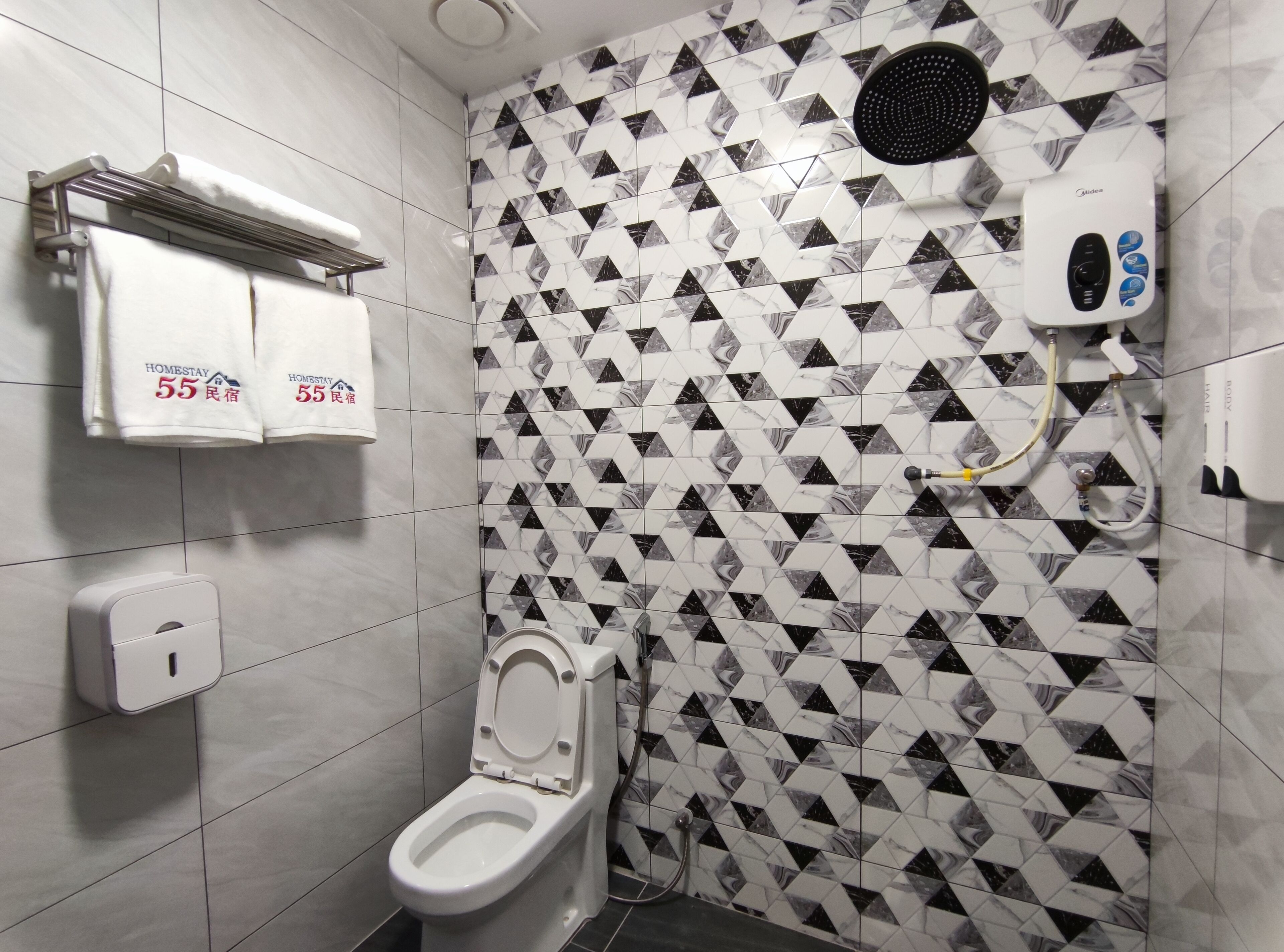 Un baño con inodoro, secamanos, toallero con toallas y dispensador de jabón.