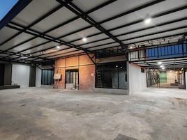 Un edificio espacioso de estilo industrial, con paredes de ladrillo visto, grandes ventanales y un techo alto con vigas de metal.