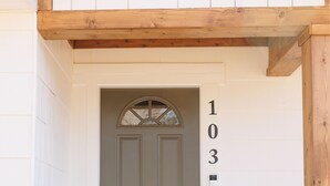 A front door with the number 103, a wooden overhang, and a doormat. - Cozy Historic District Cottage (Dothan)