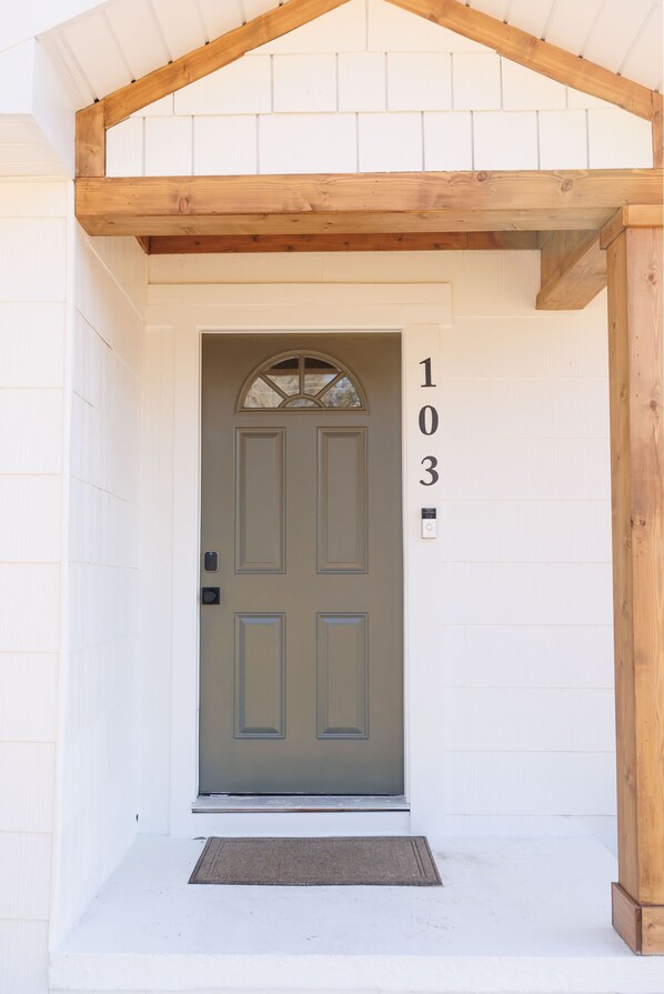 A front door with the number 103, a wooden overhang, and a doormat. - Cozy Historic District Cottage (Dothan)