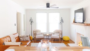 A modern living room with a sofa, two armchairs, a coffee table, a fireplace, and a TV mounted on the wall. - Cozy Historic District Cottage (Dothan)