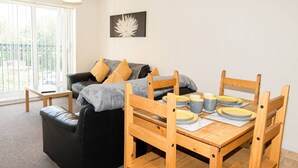 Ett mysigt vardagsrum med en soffa, ett matbord i trä som är dukat med tallrikar och koppar, och ett stort fönster med persienner.
