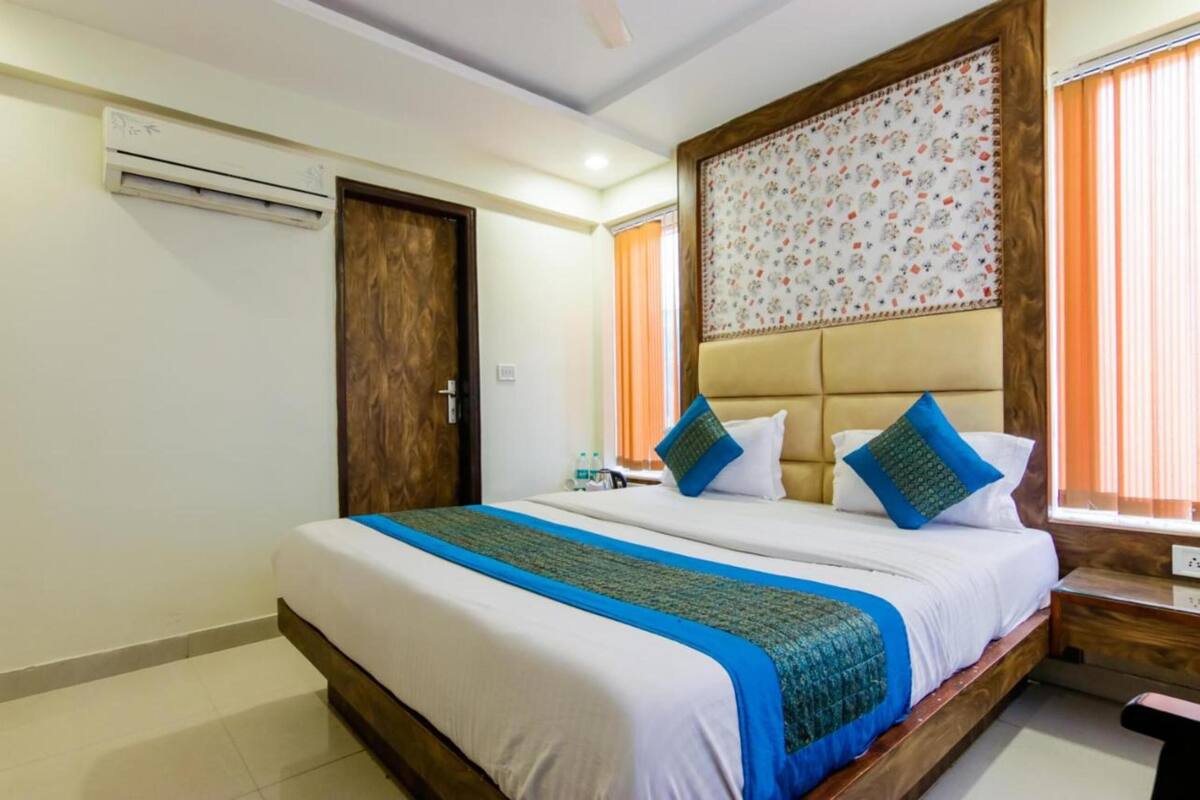 Habitación de hotel con una cama grande, cabecera de madera, unidad de aire acondicionado, una puerta y una ventana con cortinas.