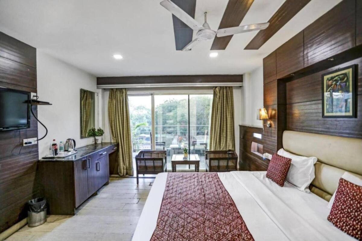 Habitación de hotel con cama, escritorio, silla, televisión y balcón con cortinas.