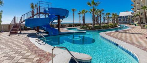 A swimming pool with a blue slide, palm trees, and a clear blue sky.