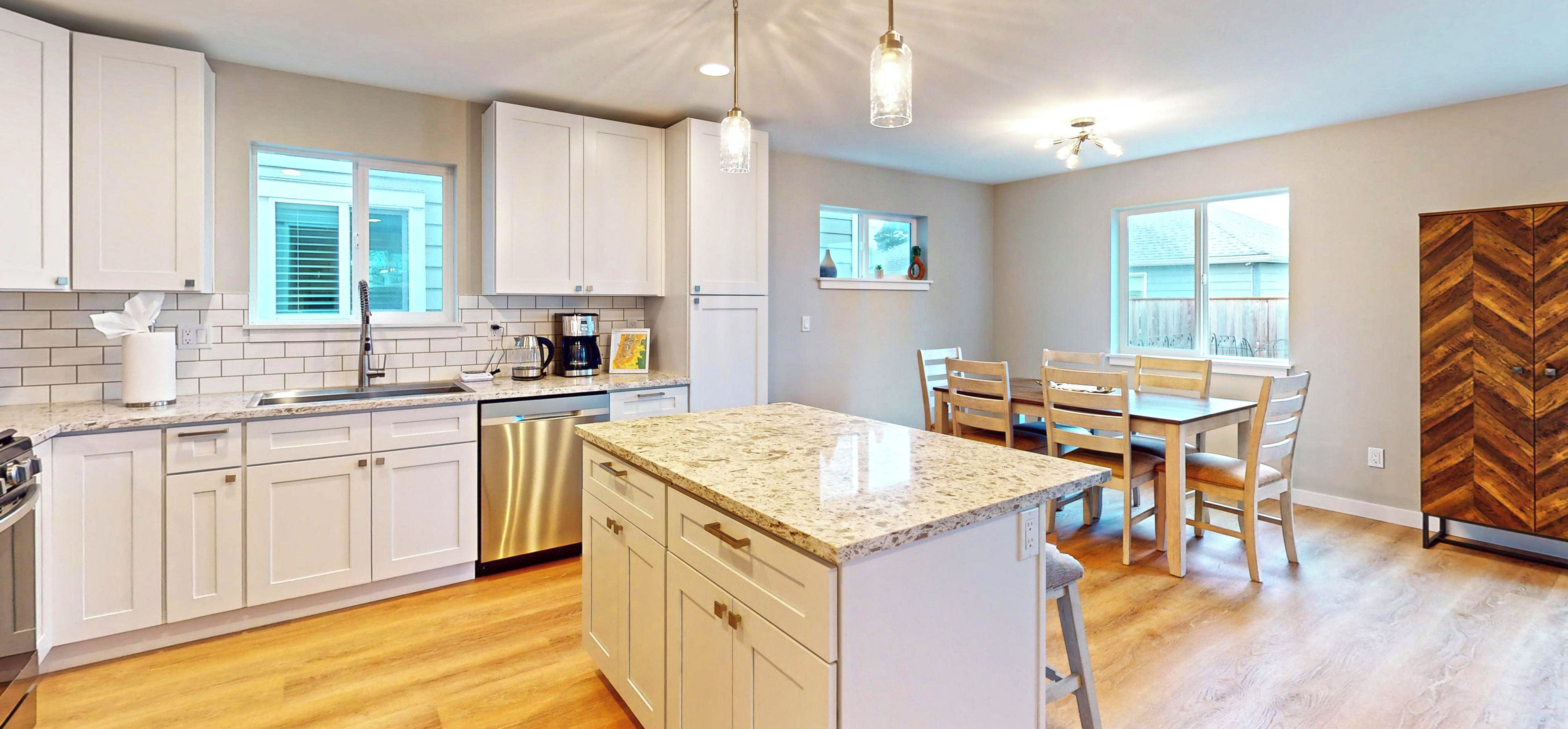 A modern kitchen with white cabinets, a granite countertop, and a dining area with wooden chairs.