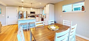 A modern kitchen with white cabinets, stainless steel appliances, and a wooden dining table with four chairs. - House Oceanic at Seaside Beach (Seaside)