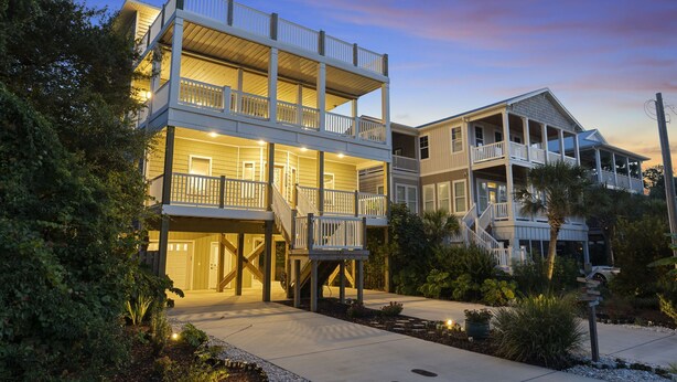 A two-story house with a balcony on the upper floor, surrounded by greenery. - Beaches Be Crazy | Dog Friendly + Game Room & Walk to Beach! (Carolina Beach)