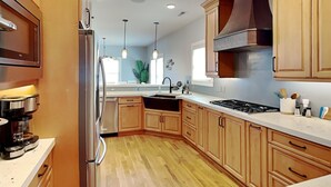 A modern kitchen with wooden cabinets, a stainless steel refrigerator, a gas stove, and pendant lighting. - Beaches Be Crazy | Dog Friendly + Game Room & Walk to Beach! (Carolina Beach)