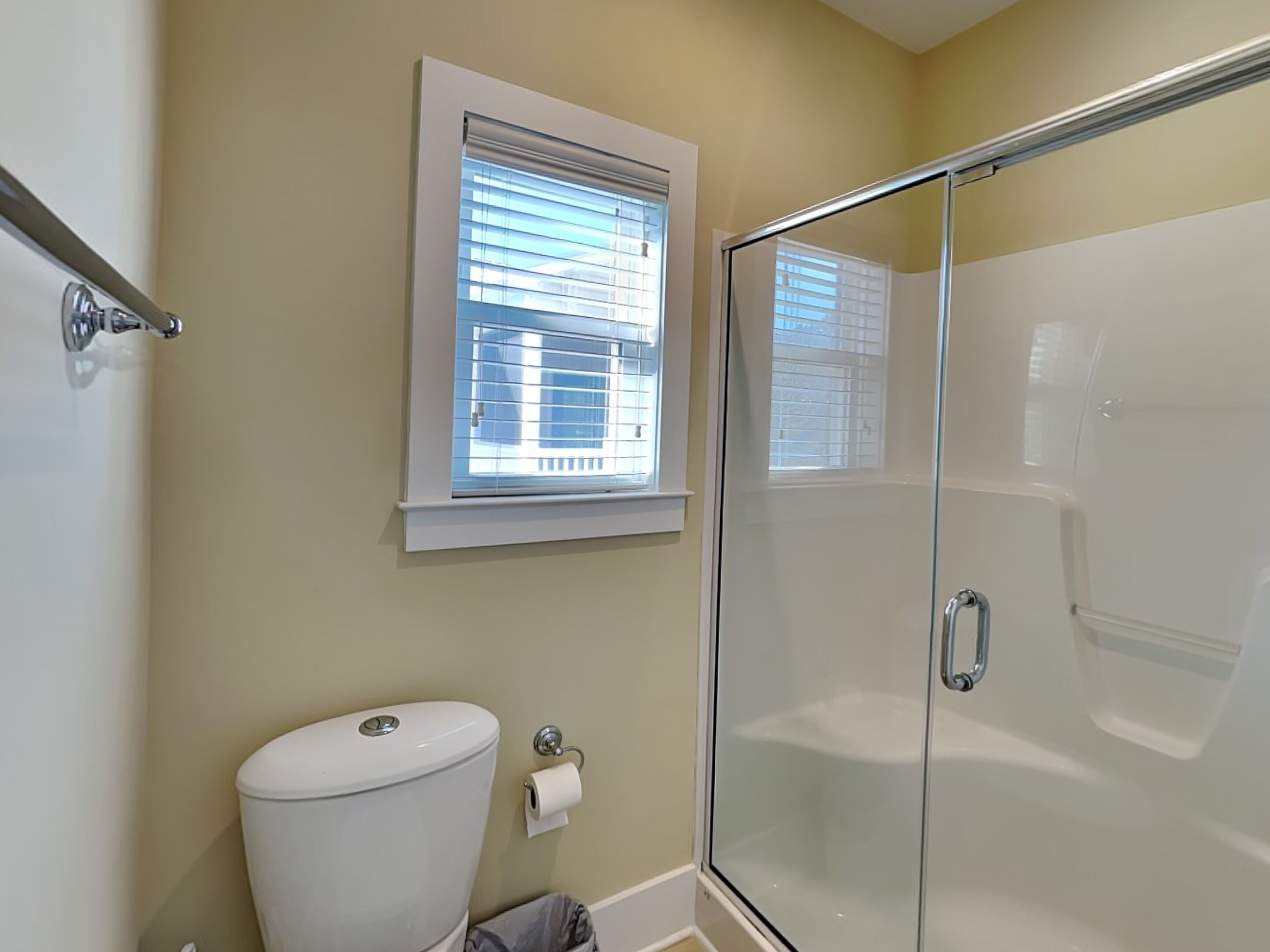 Ein Badezimmer mit Toilette, einer Duschkabine aus Glas und einem Fenster mit Jalousien.