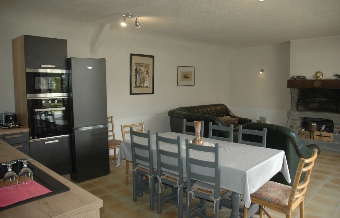 A compact living space with a kitchen area featuring a modern black refrigerator, a dining table with chairs, and a green sofa.
