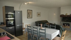 A compact living space with a kitchen area featuring a black refrigerator and oven, a dining table with chairs, a green sofa, and a fireplace. - Longère Bretonne sur Bord de Rivière (Arzano)