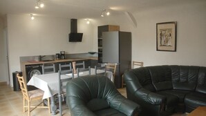 A compact living space with a dining area, a kitchen, and a seating area with a black leather sofa. - Longère Bretonne sur Bord de Rivière (Arzano)
