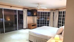 A bedroom with a large bed, a TV mounted on the wall, and a sliding glass door leading to a balcony. - Marina View Villa (Gros Islet)