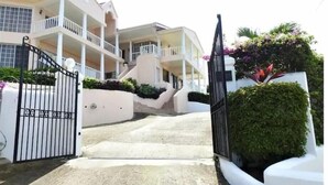 A multi-story building with a gated entrance, a staircase leading to the upper floors, and a well-maintained garden area. - Marina View Villa (Gros Islet)