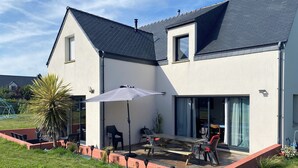 Una casa moderna con patio, un ombrellone grande e posti a sedere all'aperto.