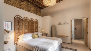 Une chambre à coucher avec un grand lit, une tête de lit en bois, un lustre et une porte menant à la salle de bain.