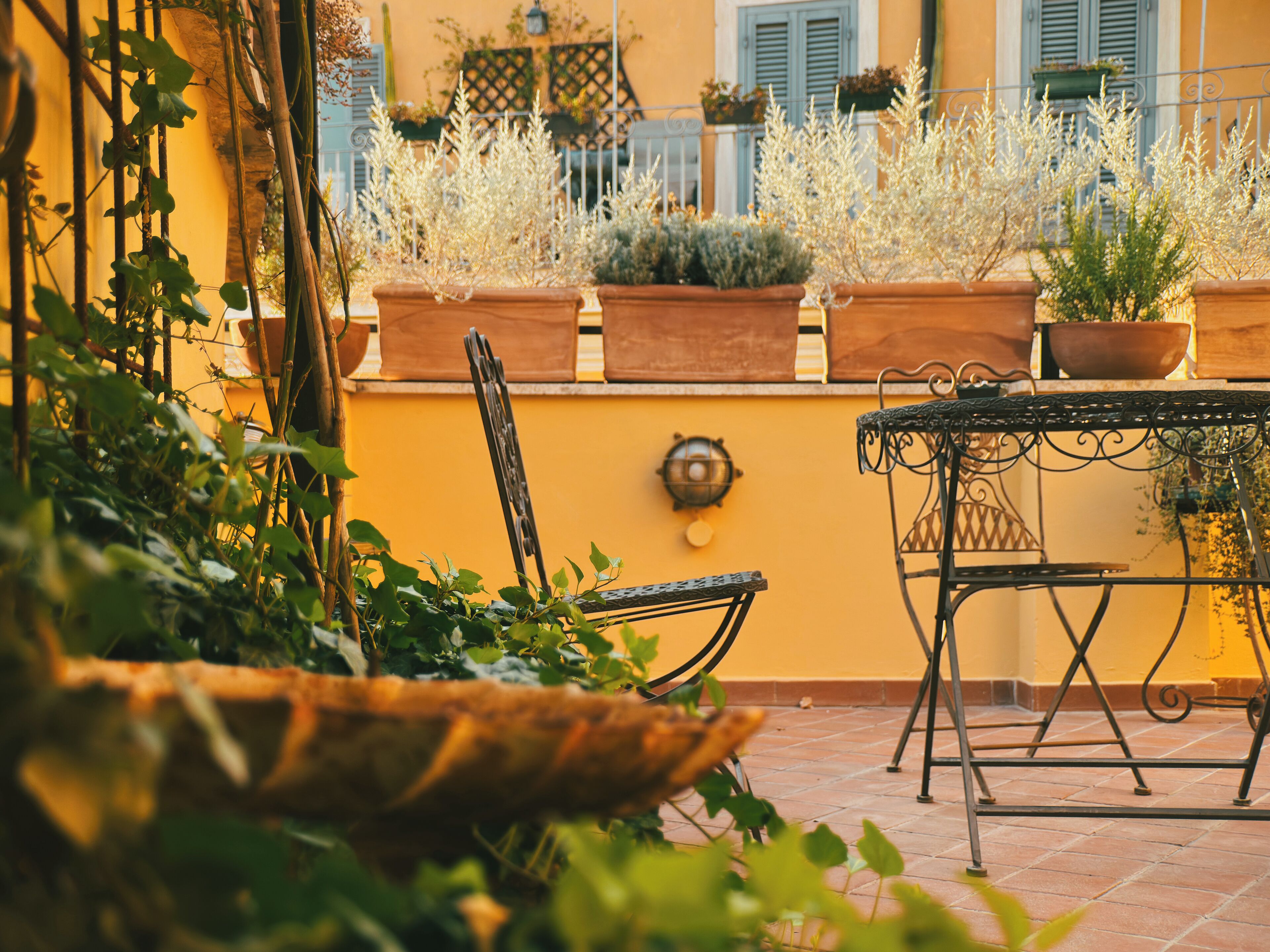 A terrace with potted plants, a metal table, and a chair.