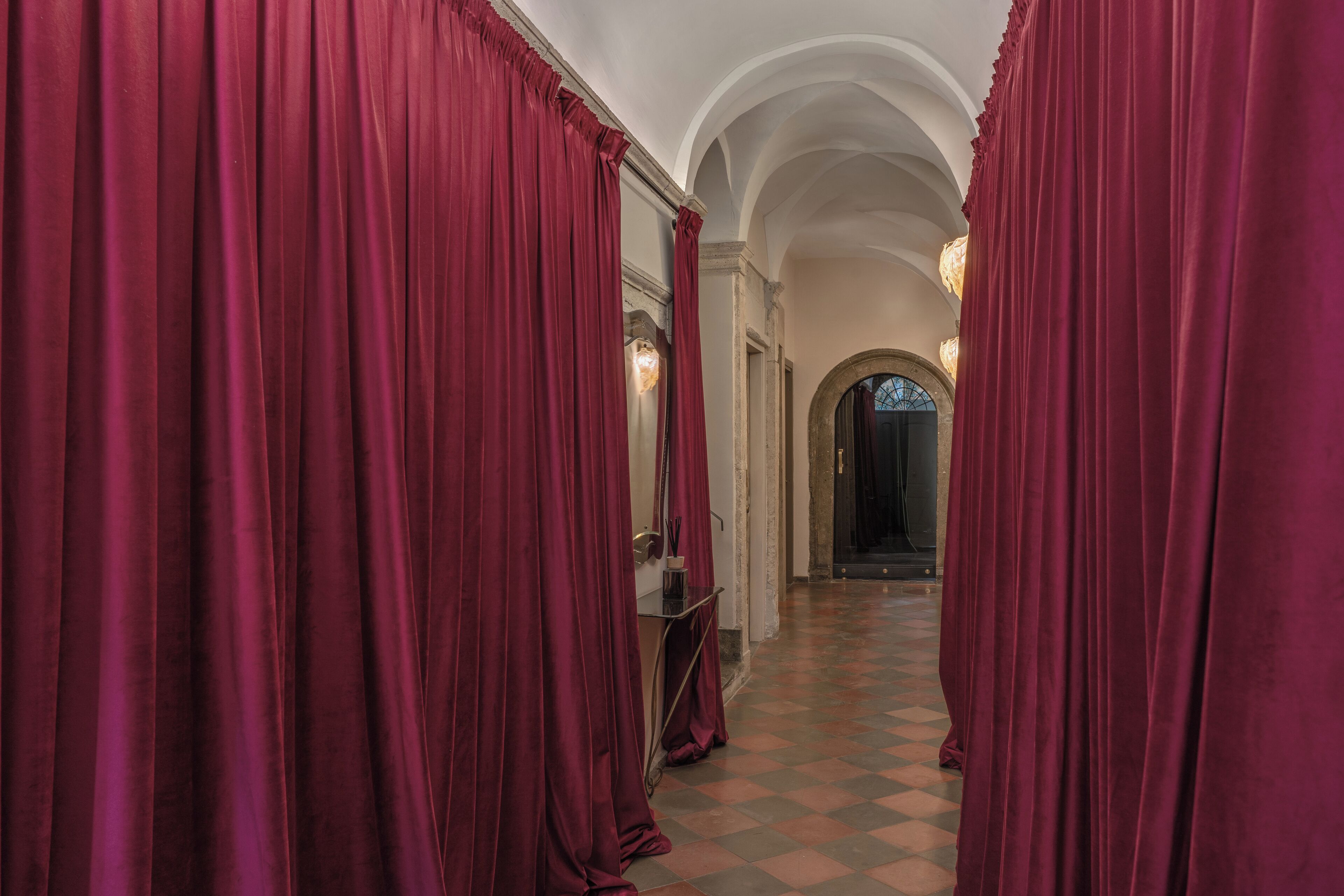 Un couloir avec des rideaux rouges, un miroir et un sol à carreaux.
