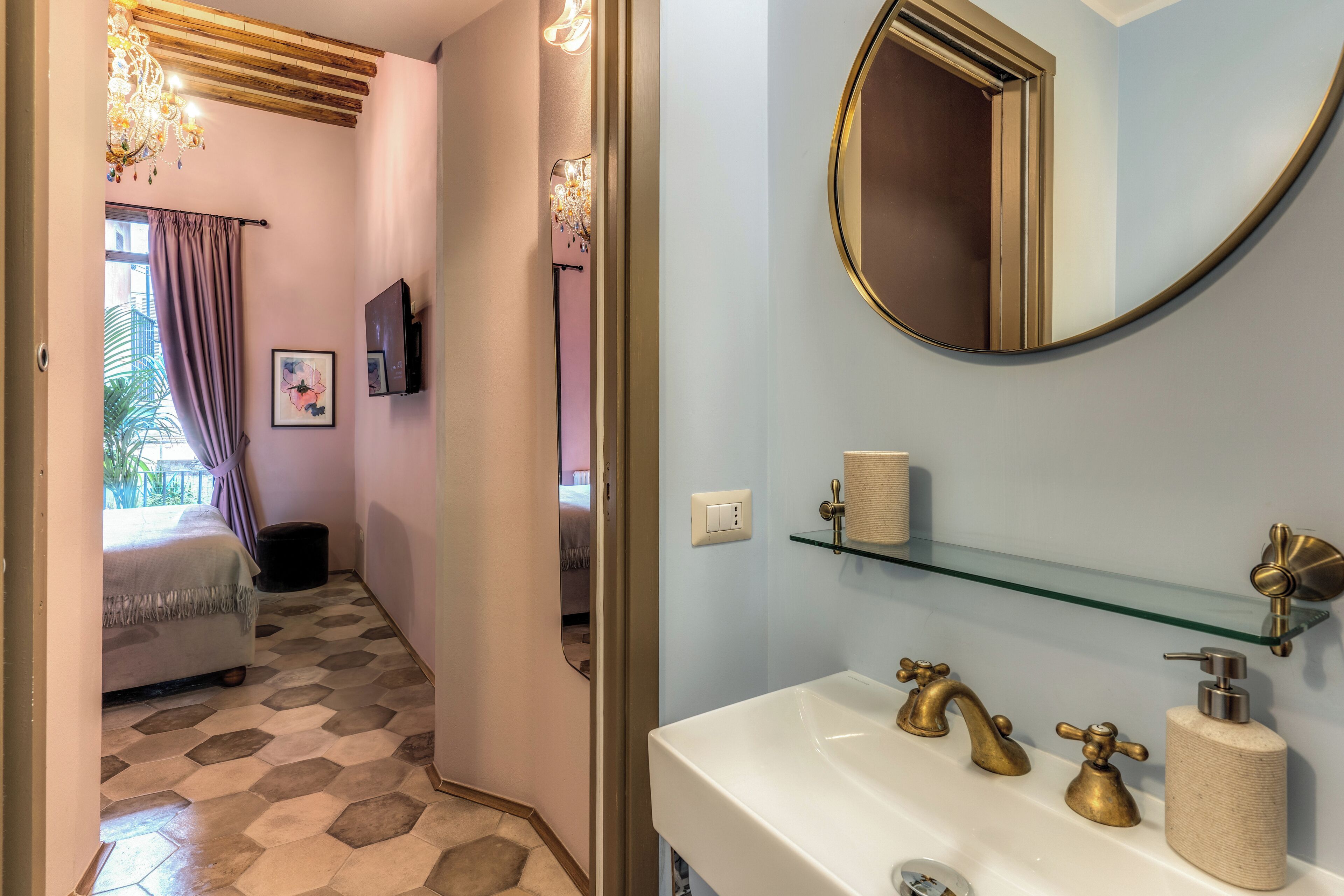 A bathroom with a white sink, gold faucets, a round mirror, and a glass shelf.