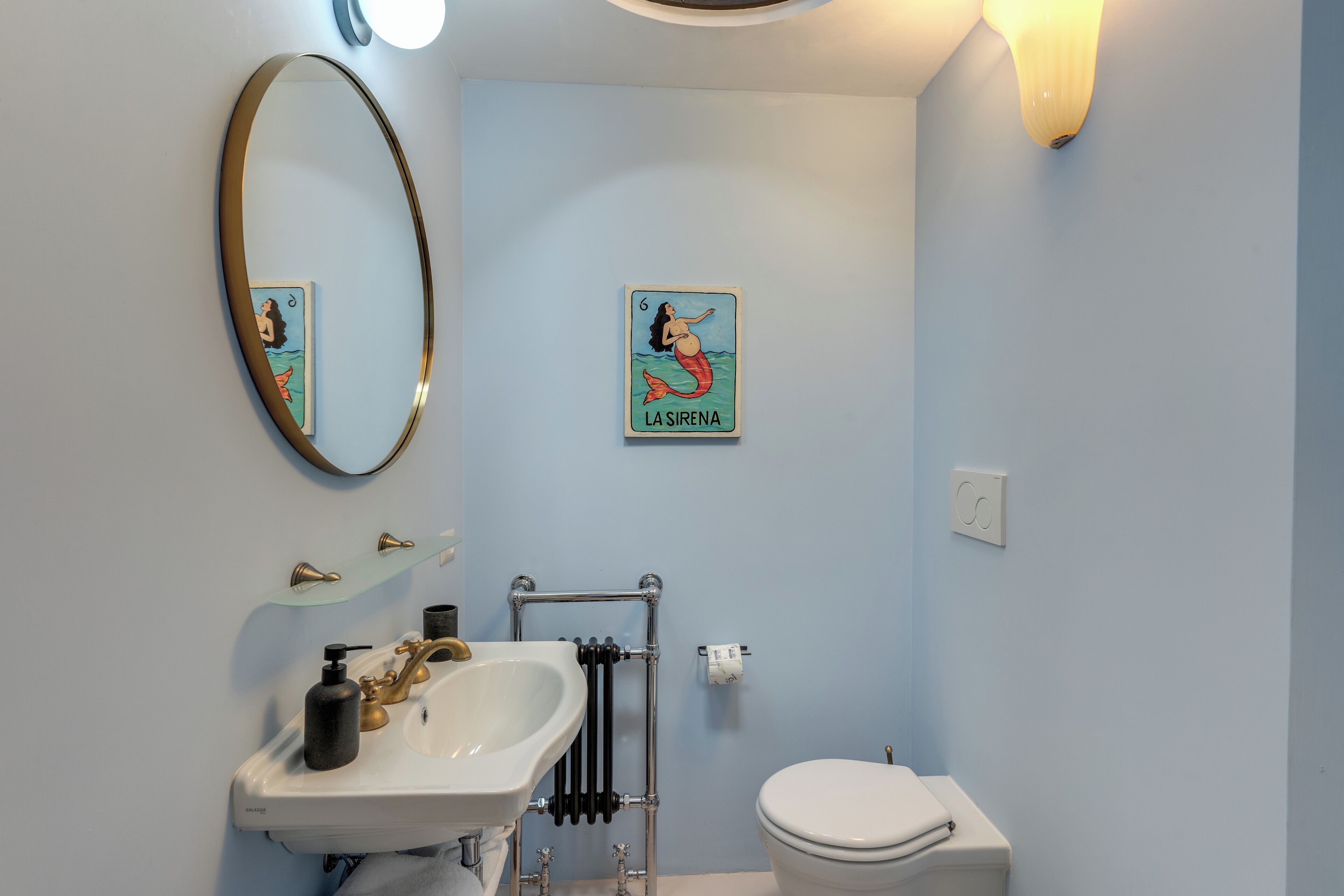 Une salle de bain avec un lavabo blanc, des toilettes, un radiateur et un miroir fixé au mur.
