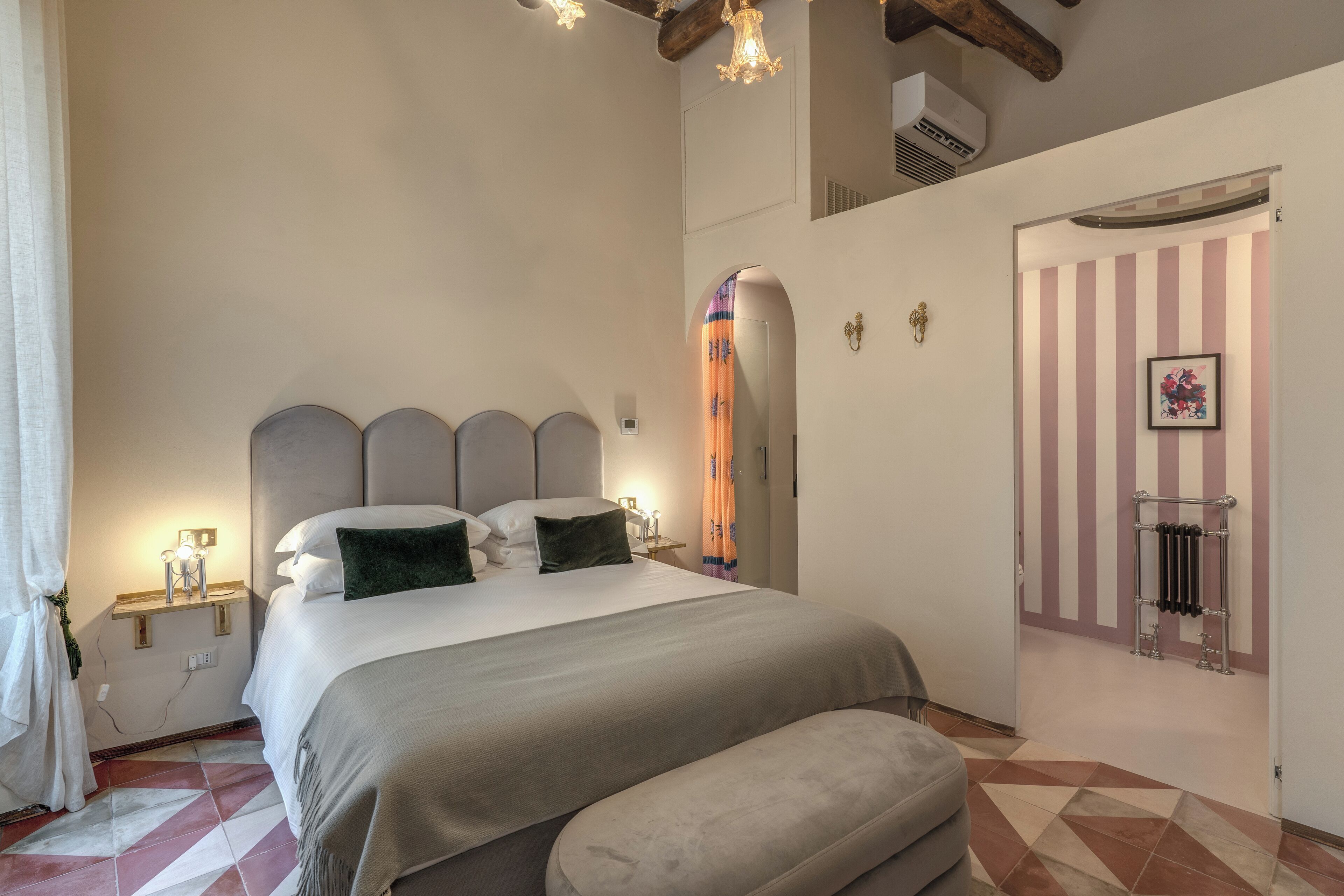 Ein Schlafzimmer mit einem Bett, Nachttischen, einer Bank, einem Heizkörper und einer Tür, an deren Wand sich Streifen befinden.