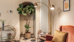 Un salon chaleureux avec une grande plante, un lampadaire, un fauteuil rouge et une bibliothèque.