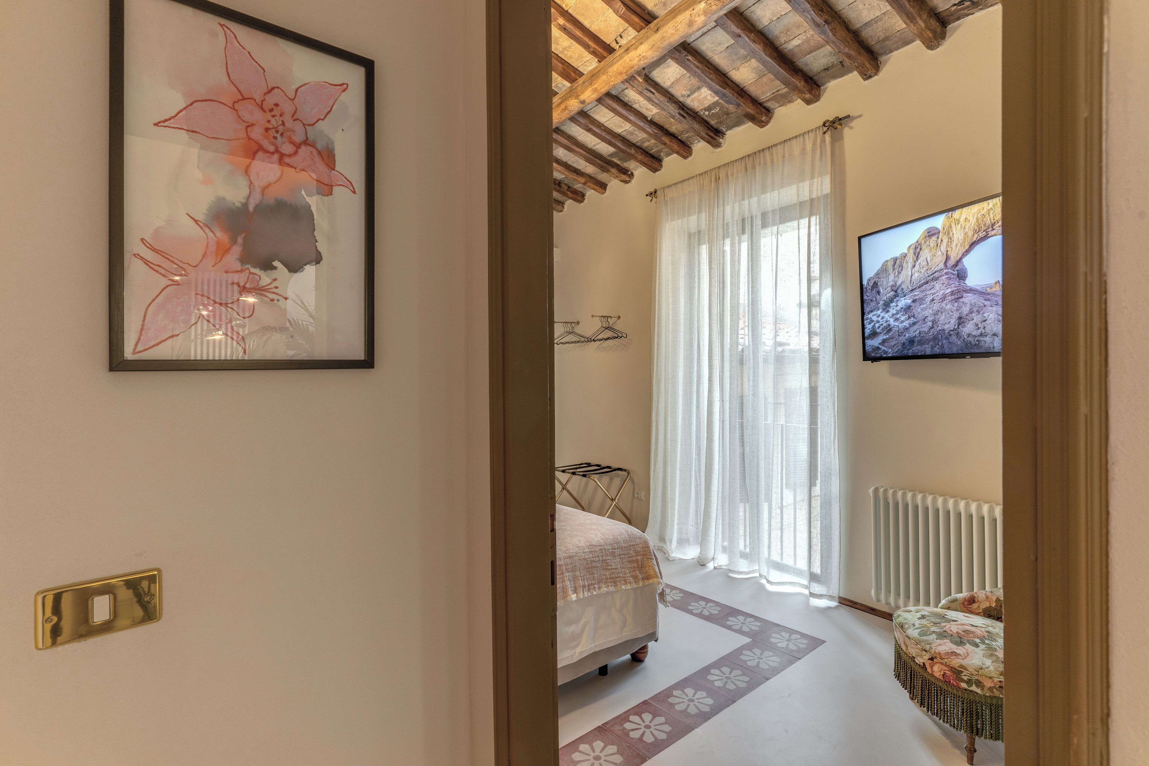 A bedroom with a bed, a TV, a radiator, and a window with curtains.