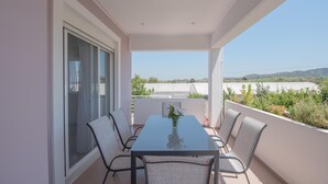 Een balkon met een glazen tafel en stoelen, uitzicht op het landschap, en een witte muur.