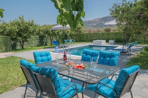 A poolside area with a glass table, blue cushioned chairs, and a view of the mountains.