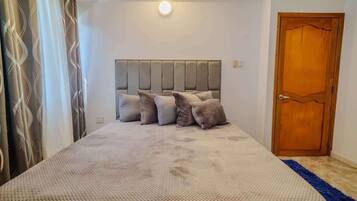 A bedroom with a large bed, a headboard, and a wooden door.