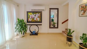 A spacious living area with a large potted plant, a framed artwork, and a staircase leading to another level.