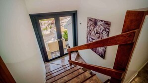 A wooden staircase leading to a glass door with a view of a garden and a lion painting on the wall.