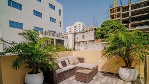 A rooftop patio with a wicker sofa and two potted plants.