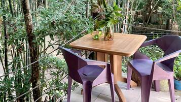 Una mesa de madera con dos sillas moradas, rodeada de abundante vegetación.