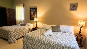 Habitación de hotel con dos camas, cada una con ropa de cama estampada, una mesita de noche con lámpara, un cuadro en la pared y un equipo de aire acondicionado.