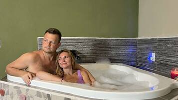 Una pareja en un jacuzzi con mosaicos y una pared de piedra.