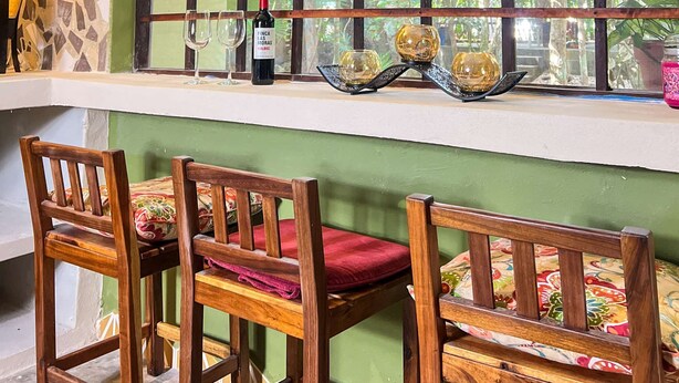 Una habitación con un ventanal grande, sillas de madera, una mesa y una botella de vino.