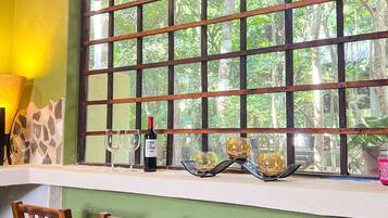 Una habitación con un ventanal grande, sillas de madera, una mesa y una botella de vino.