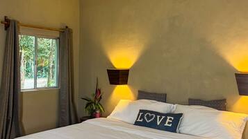 Un dormitorio con cama, ventana con cortinas, lámpara de pared y almohadón decorativo con la palabra 'LOVE'.