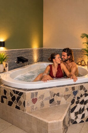 Una pareja en un jacuzzi con paredes de mosaicos y un azulejo con forma de corazón.
