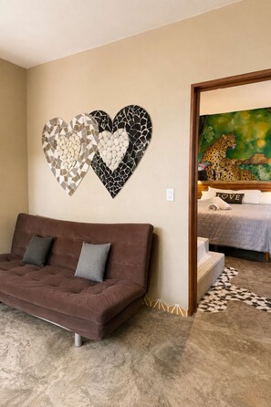 Una sala de estar con un sofá marrón, dos piezas de arte mural con forma de corazón y un cuadro con la imagen de chitas en la pared.