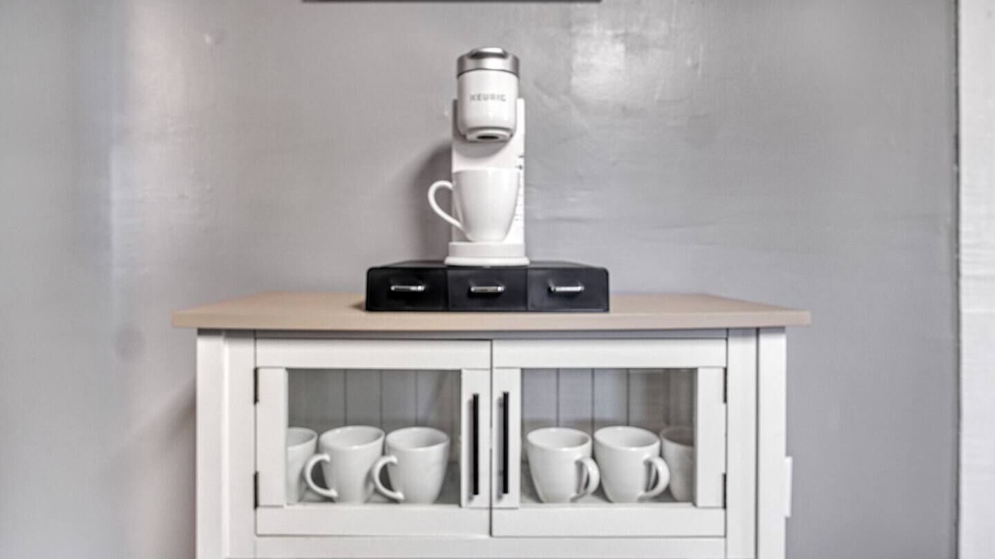 Ein weißer Schrank mit einer Kaffeemaschine darauf und mehreren weißen Tassen darin.