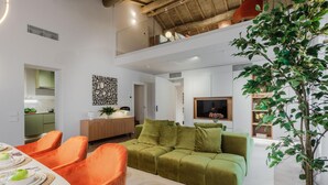 A modern living room with a green sofa, orange chairs, and a dining table set for a meal. - The Victory Penthouse (Lucca)
