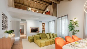 A spacious living area with a high ceiling, a green sectional sofa, orange chairs, and a dining table set for four. - The Victory Penthouse (Lucca)