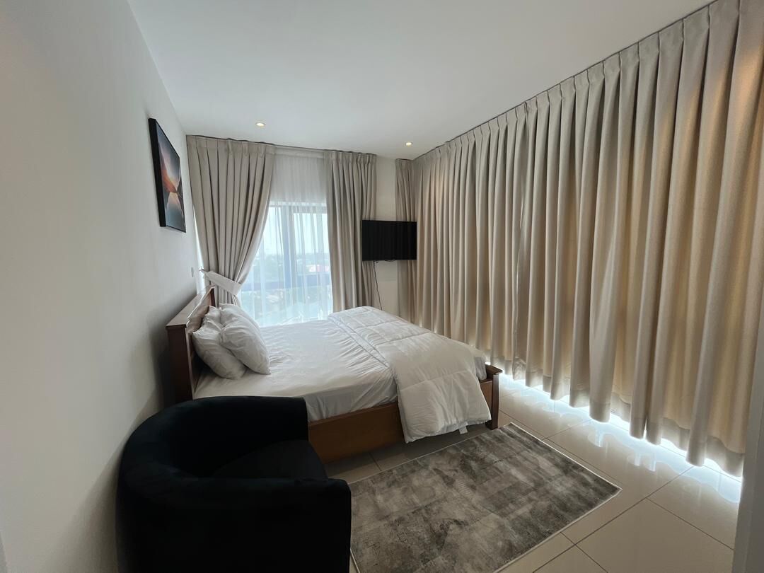 A modern bedroom with a bed, a TV mounted on the wall, and large curtains.